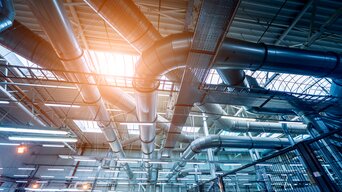 Lüftungsrohre in der Höhe eines großen grauen industriellen Raumes