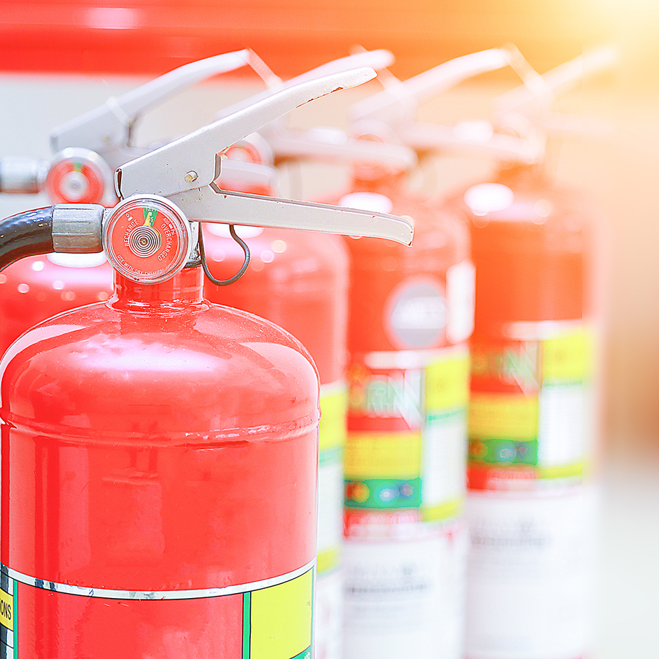 Mehrere Feuerloescher vor einem weiß-rot-orangen Hintergrund. | © A Stockphoto - AdobeStock