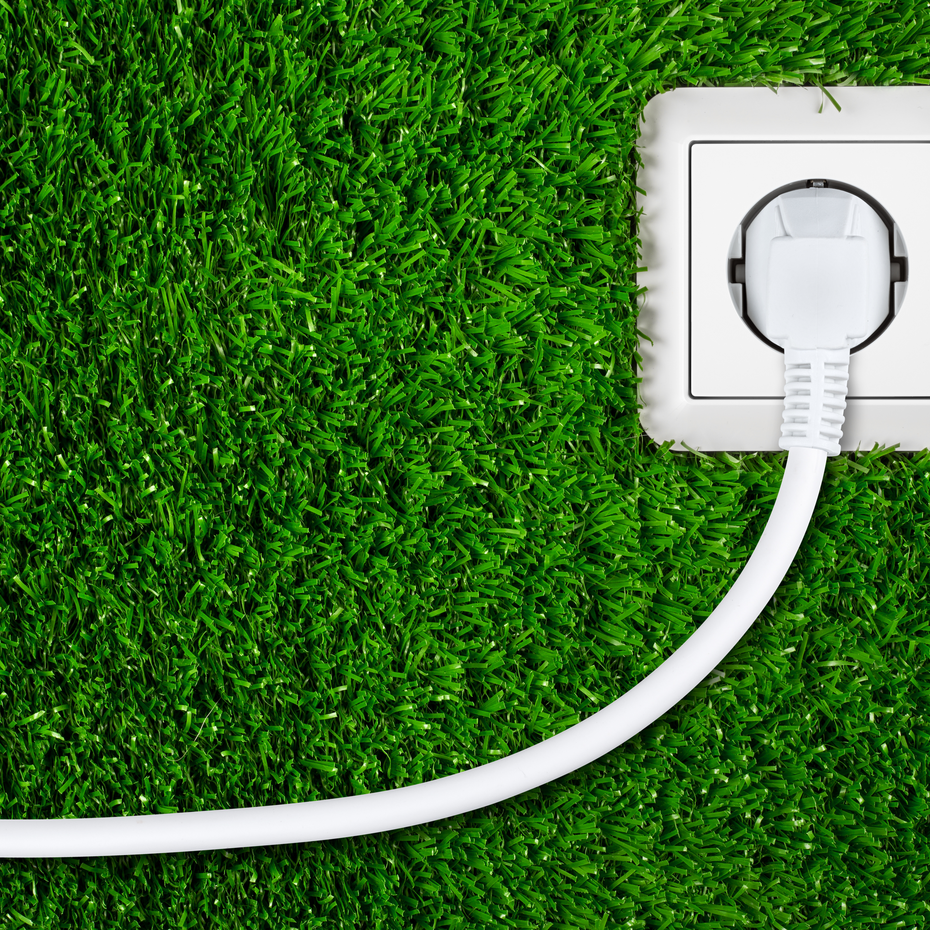 Weiße Steckdose mit eingestecktem Kabel auf grünem, natürlichem Gras als Symbol für nachhaltige Energie | © stockphoto-graf - stock.adobe.com