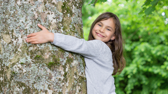 Kind umarmt Baum und lächelt in die Kamera