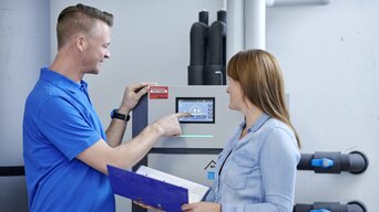 Techniker erklärt einer Kundin die Bedienung einer modernen bösch Heizungsanlage in einem Technikraum | © bösch heizung.klima.lüftung
