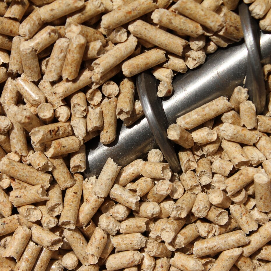 Nahaufnahme von Holzpellets mit einer Schnecke aus Metall, die zur Förderung der Pellets verwendet wird.