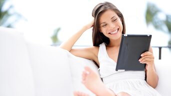 Frau entspannt auf einem weißen Sofa und nutzt ein Tablet | © Maridav - Fotolia