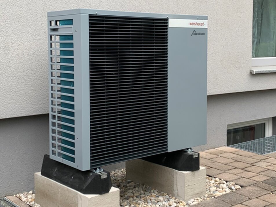 Außenaufgestellte Wärmepumpe an einem Mehrfamilienhaus, installiert auf stabilen Fundamentblöcken | © bösch