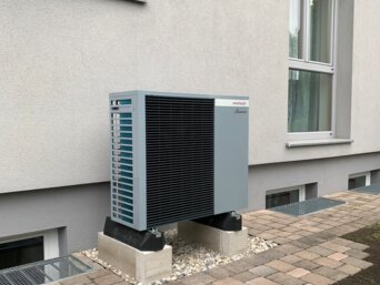 Außenaufgestellte Wärmepumpe an einem Mehrfamilienhaus, installiert auf stabilen Fundamentblöcken | © bösch