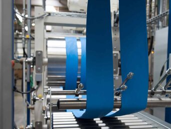 Produktionsmaschine von Kraiburg TPE, die blaue Kunststoffbänder verarbeitet. Sichtbar sind Walzen und Führungsmechanismen, die die Bänder in der Maschine bewegen | © Kraiburg TPE, Germany