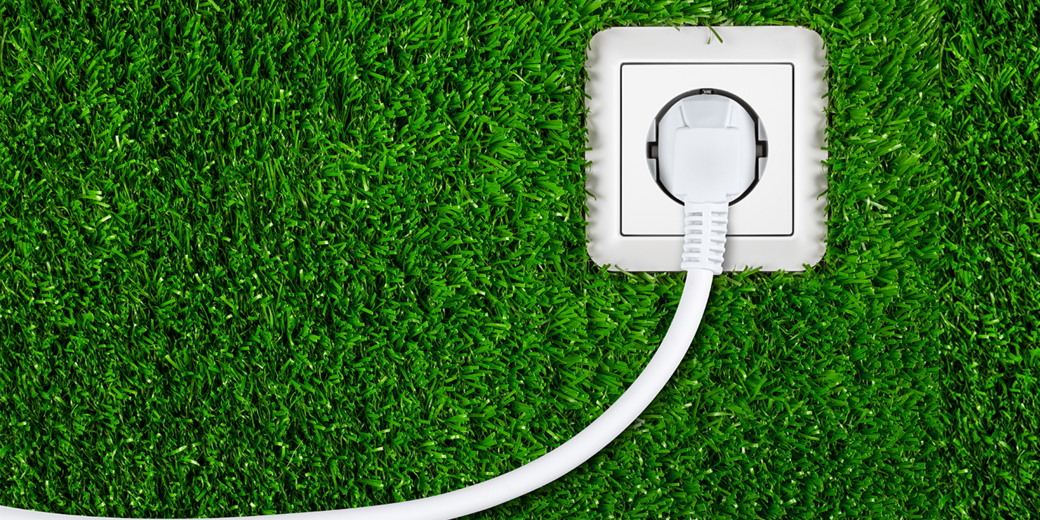 Weiße Steckdose mit eingestecktem Kabel auf grünem Rasenteppich – Symbol für nachhaltige Stromnutzung und Energiekosten bei Wärmepumpen