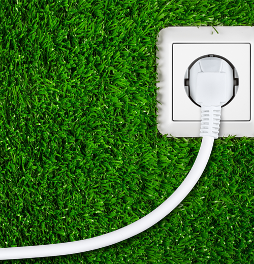 Weiße Steckdose mit eingestecktem Kabel auf grünem Rasenteppich – Symbol für nachhaltige Stromnutzung und Energiekosten bei Wärmepumpen