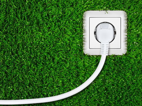 Weiße Steckdose mit eingestecktem Kabel auf grünem Rasenteppich – Symbol für nachhaltige Stromnutzung und Energiekosten bei Wärmepumpen