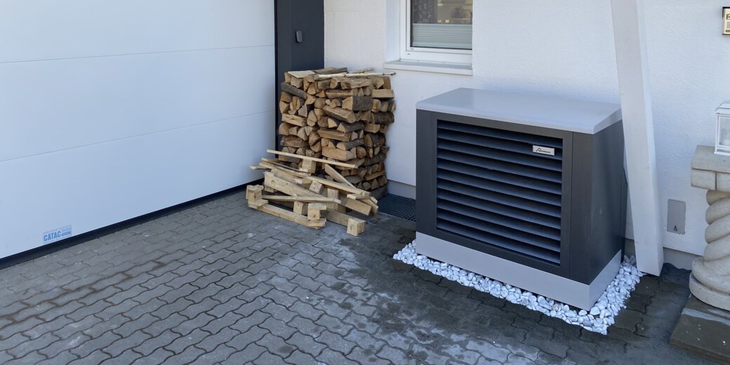 Außen aufgestellte Wärmepumpe von bösch neben einem Holzlager – eine sorgenfreie Heizlösung mit stilvollem Design direkt vor dem Haus