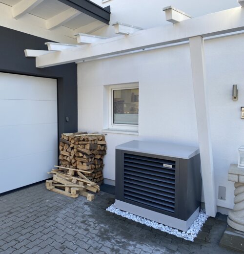 Außen aufgestellte Wärmepumpe von bösch neben einem Holzlager – eine sorgenfreie Heizlösung mit stilvollem Design direkt vor dem Haus