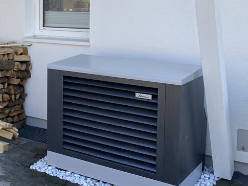 Außen aufgestellte Wärmepumpe von bösch neben einem Holzlager – eine sorgenfreie Heizlösung mit stilvollem Design direkt vor dem Haus