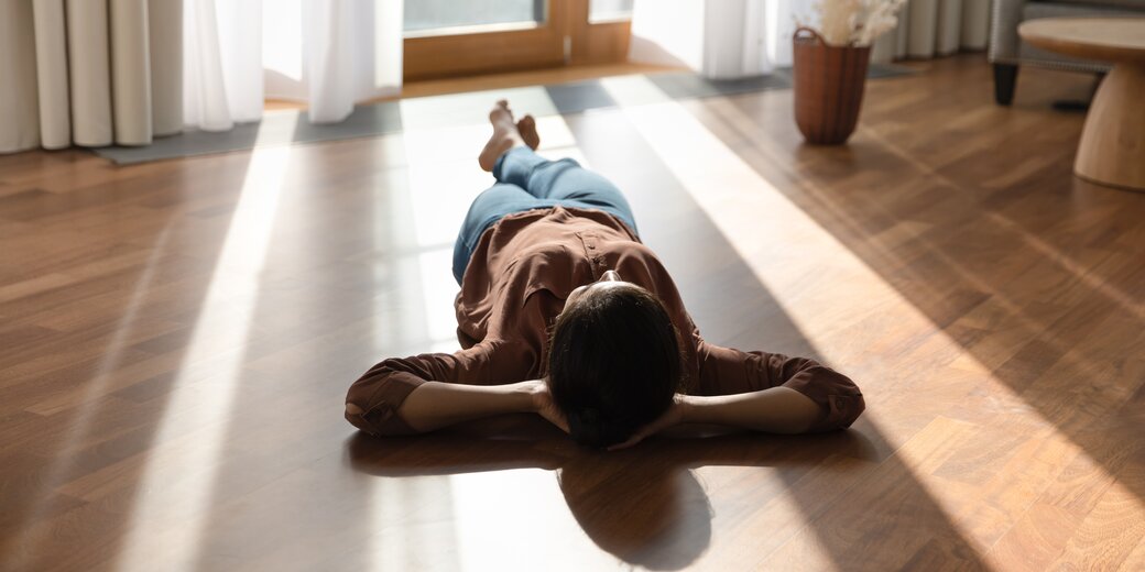 Person liegt entspannt auf sonnigem Holzboden – Symbol für behagliche Wärme durch Fußbodenheizung mit Wärmepumpe