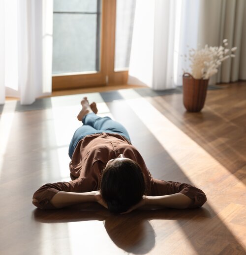 Person liegt entspannt auf sonnigem Holzboden – Symbol für behagliche Wärme durch Fußbodenheizung mit Wärmepumpe