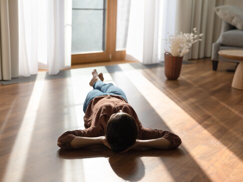 Person liegt entspannt auf sonnigem Holzboden – Symbol für behagliche Wärme durch Fußbodenheizung mit Wärmepumpe